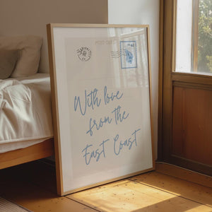 with love from the east coast in blue script typography on vertical postcard print with seashell stamp