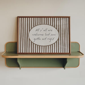 all y'all are welcome but you gotta act right quote in hand drawn script typography on brown striped wall art with oval cutout, horizontal wall art for western decor